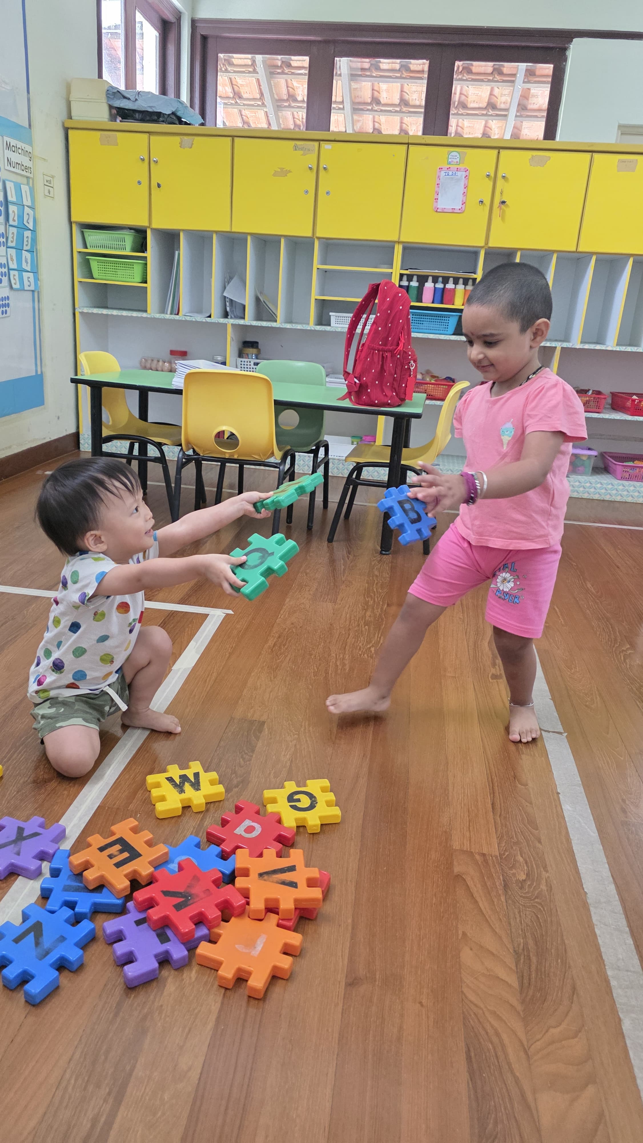 Two children sharing and playing with letter puzzle pieces at Genius Gems Childcare Centre